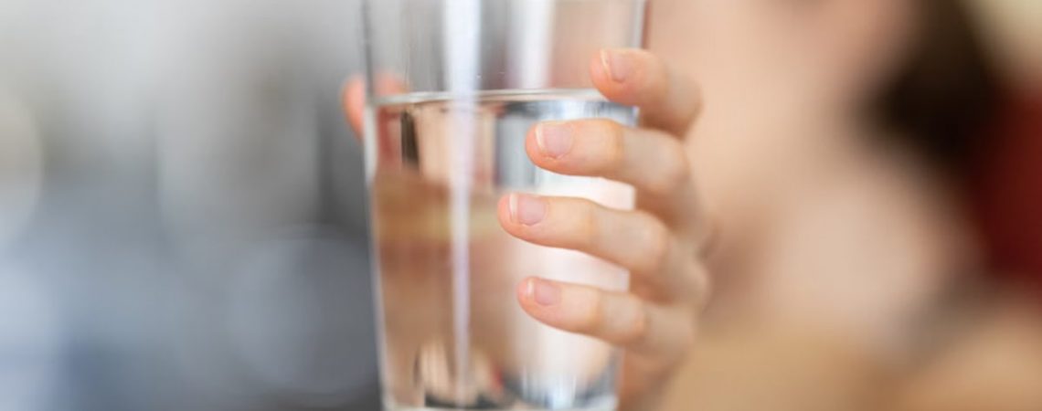 A hand holding a clear glass of water with a blurred background for health and hydration concept.