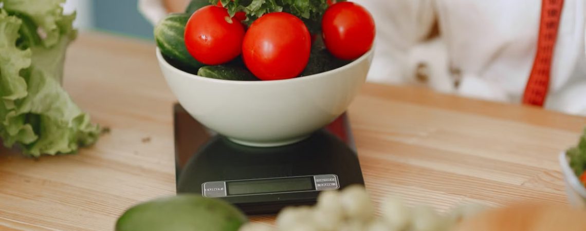 Colorful fresh vegetables including tomatoes and cucumbers on a kitchen scale for healthy eating.